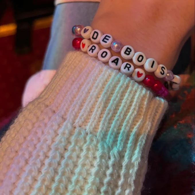 A hand with friendship bracelets on reading: DE BOIS and ROAR.