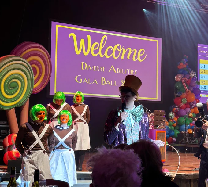 Event compere dressed as Willy Winka supported by people dressed as Oompah Loompahs walking among the tables