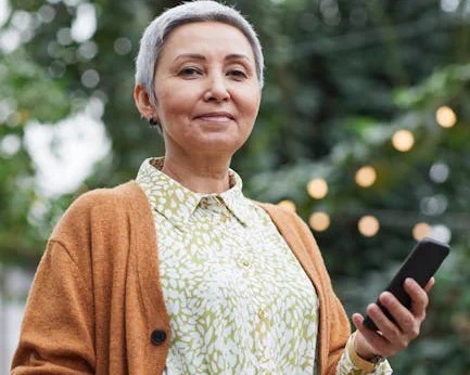 Cheerful senior woman in a garden holding a smartphone, embracing technology and connectivity.