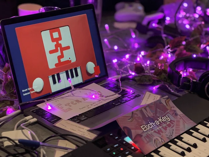 A photograph from game-a-week party. One of the games being showcased that uses a keyboard for input with pink fairy lights strewn across the table.