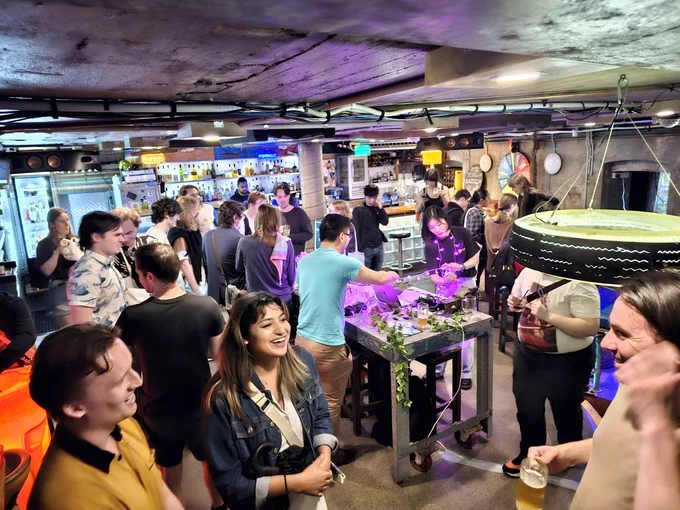 A photograph from game-a-week party. A handfull of people talking and smiling in a quaint and vibey bar.