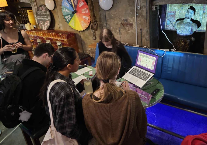 A photograph from game-a-week party. A cluster of people playing a game together with it's image projected onto a statue behind.