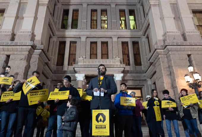 Picture from the 2018 World Day of Remembrance for Road Traffic Victims on the South Steps of the Texas State Capitol with Jay Blazek Crossley standing at the mic with a crowd of people holding yellow signs that say Crash Not Accident and similar messages.

Photo by Joe Van Wyk