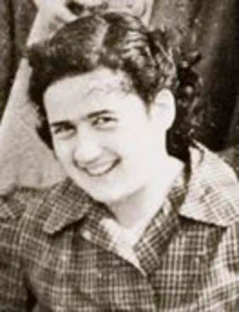 A young woman smiling. She was checked blouse and dark curly hair.