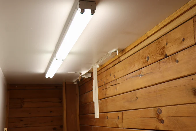 A fluorescent light illuminates a storage room on the Oglala Lakota campus where paint on the ceiling is peeling in long white strips due to a leak.