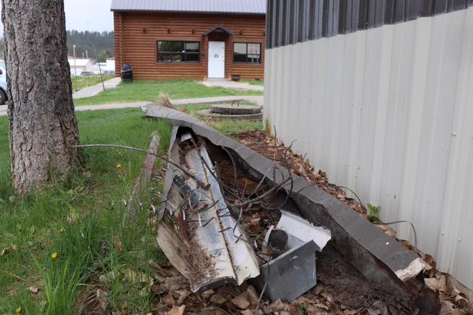 Multiple pieces of metal, bent out of shape, lie on the ground next to a Chief Dull Knife College building.