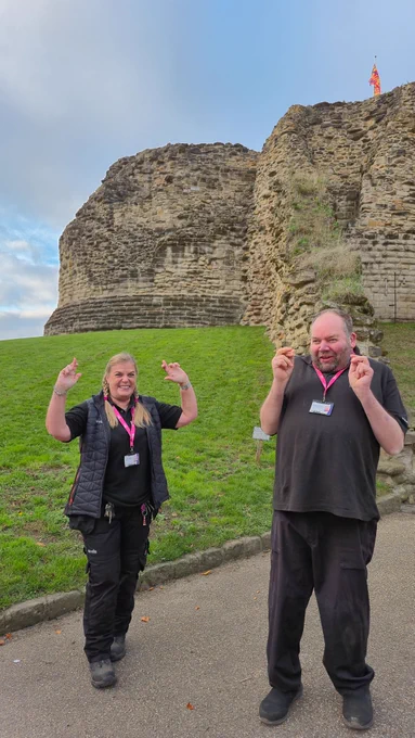 Joe and Michael grinning and holding up their crossed fingers in front of the keep at Pontefract Castle