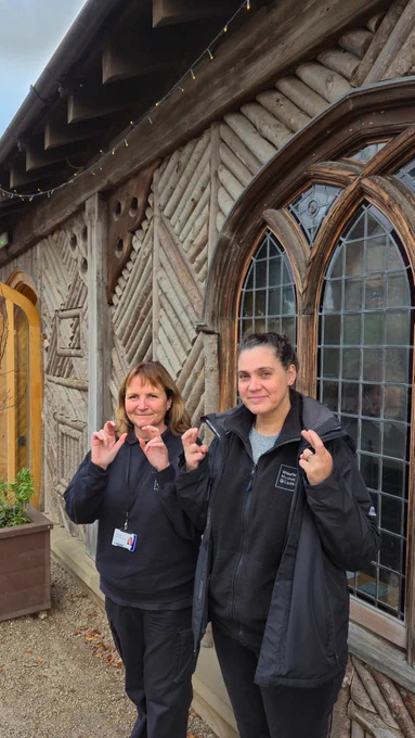 Joan and Stacey smiling and holding up their crossed fingers in front of the Visitor Centre at Pontefract Castle