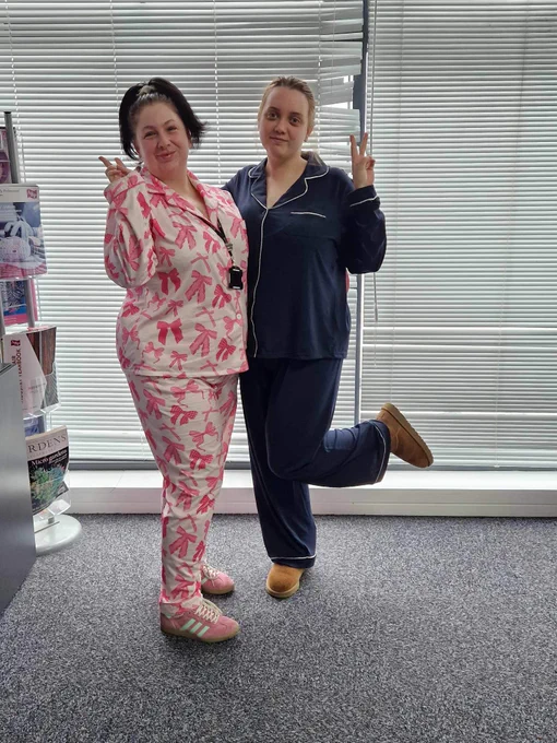 Two women stood smiling and posing in full pyjamas in Vizion Network's office space in The Deep Business Centre. 