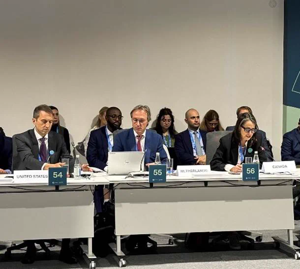 A formal meeting with delegates from different countries seated at a long table.