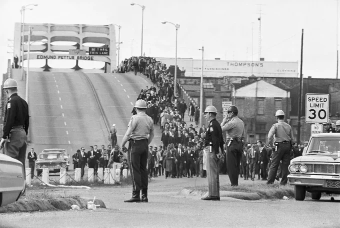 State troopers watch as marchers cross the Edmund Pettus Bridge over the Alabama River in Selma, Alabama as part of a civil rights march on March 9. Two days before troopers used excessive force driving marchers back across the bridge, killing one protester. Photo via Getty Images.
