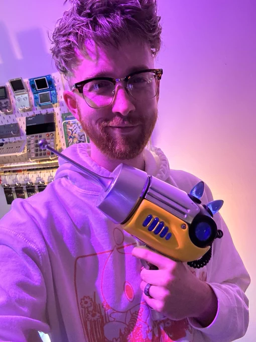 Caleb in a hoodie with a Chao from sonic on it holding the Ripple Gun, a yellow, chrome, and black sci-fi raygun with an antenna for the barrel and blue lights on the top and sides.