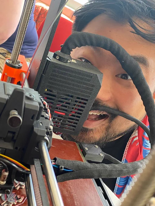 Person peering through a 3D printer with a joyful expression.
