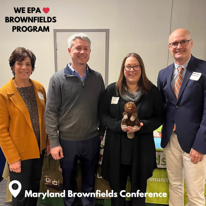 Group of people smiling with text that reads WE heart emoji EPA brownfields program. Pin emoji Maryaldn Brownfields Conference. In the photo are Susan Spielberger, Dave Campbell,  Dawn Farver and Craig Anderman from the Brownfields program with Bucky, a stuffed animal, the TAB mascot. 