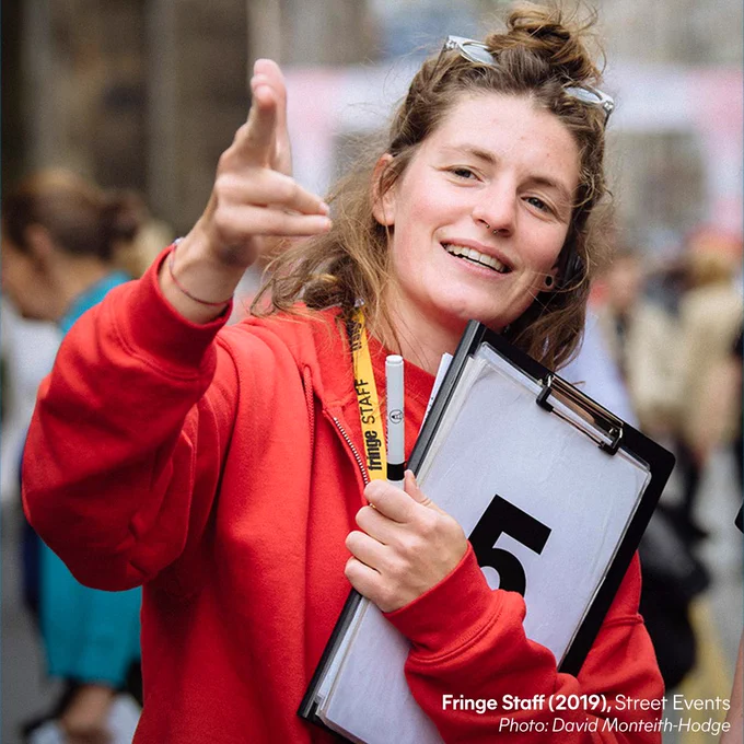 A member of the Fringe street events team holds a clipboard and points off-camera.