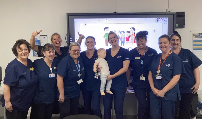 A group of nurses holding a small child mannequin in a classroom