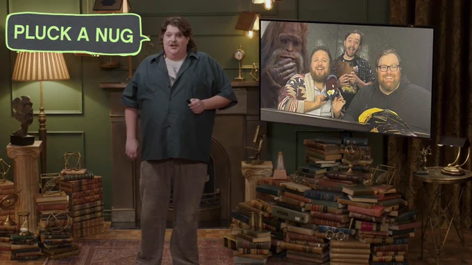 Jacob Wysocki is standing next to a screen with the boys on it. There's a mysterious big footed figure behind them. Or is there? (There is). Jacob says 'Pluck A Nug'.