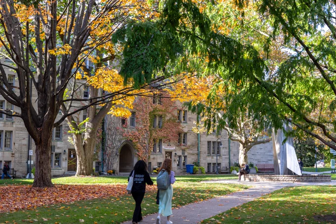 Two students walk along a leaf laden path on the St George campus during fall. 