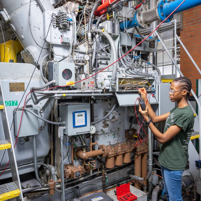 A person inspecting a cable going into a large machinery.