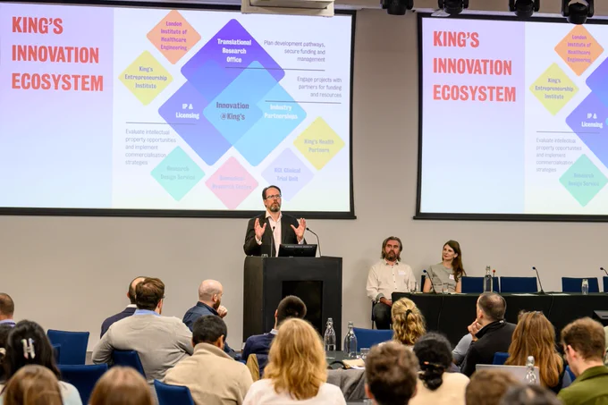 Dr Mike Shaw, Director of King's Innovation Catalyst, on stage with two slides depicting King's innovation ecosystem.