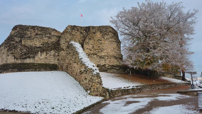 The remains of the keep at Pontefract Castle with a dusting of snow, and a large tree that has mostly lost its leaves also coated in white