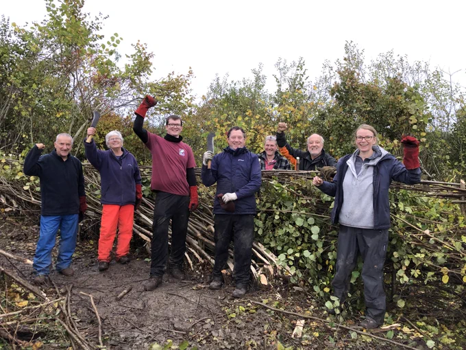 A group of people stand in front of a hedge.