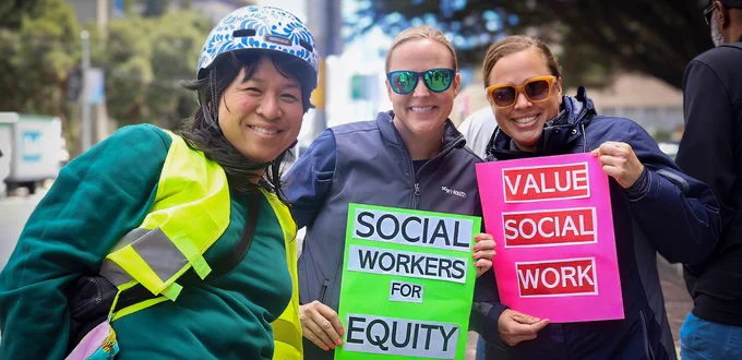 Three women hold signs saying “Social Workers for Equity” and “Value Social Work”
