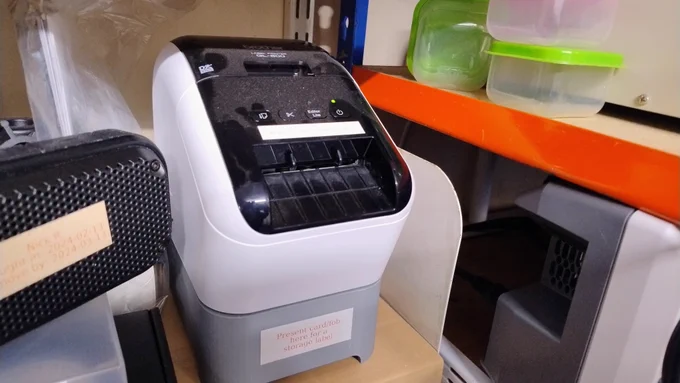 A Brother QL800 label printer sitting on a 3D printed base. You can't see from the photo but it has a Raspberry Pi print server and RFID reader inside. It's all quite dusty, because Hackspace.