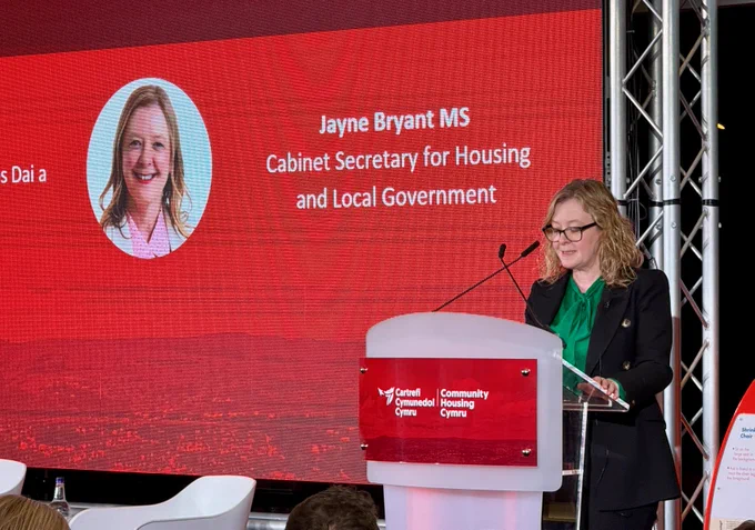Ysgrifennydd y Cabinet yn siarad ar lwyfan yng Nghynhadledd Cartrefi Cymunedol Cymru.