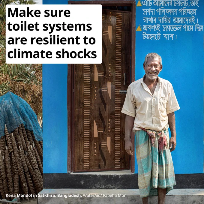 A man stands in front of a blue toilet complex in Bangladesh. 