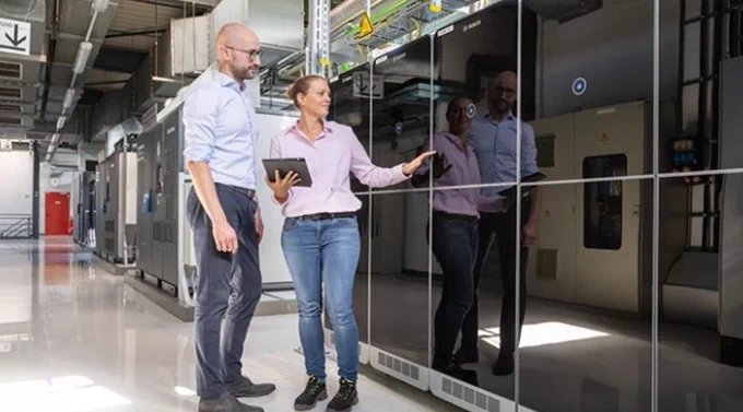 Two professionals in a data center, standing next to server racks; one person holding a tablet.