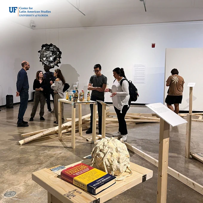 Three groups of attendees are chatting and engaging with separate artworks in the large gallery space. The artworks are connected with wooden boards spanning the floor.