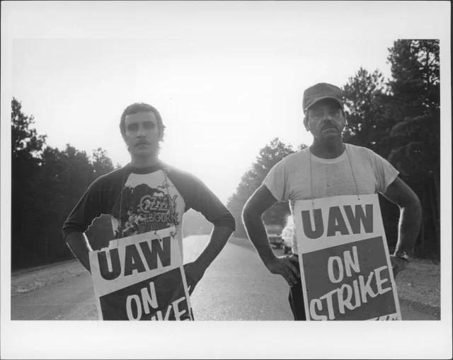 UAW Local 2216 striking members Mark Easley, 21, and Robert Rosenbaum, Sr., 52, stand in the blaze of the sun as temperatures climb into the 100s. 