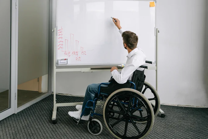 Person in a wheelchair writing on a whiteboard.