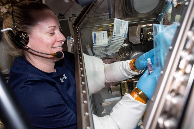 iss064e020036 (Jan. 5, 2021) --- NASA astronaut Kate Rubins uses an enclosed glovebox to conduct an experiment. Rubins is wearing a navy shirt and a headset. Her arms are elbow-deep         in the glovebox, protected with plastic covering and medical gloves.