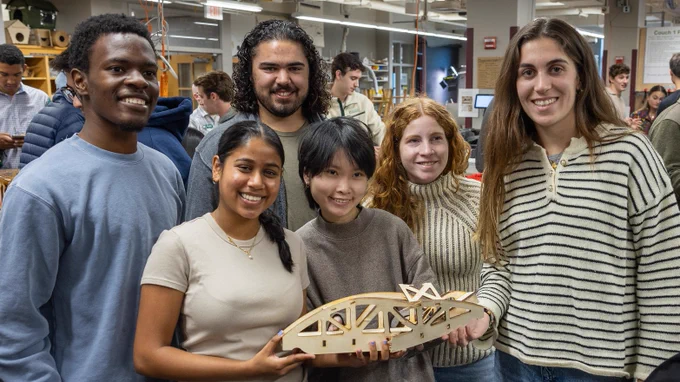 Six students smiling and standing together while holding their broken wooden bridge that they designed and tested. 