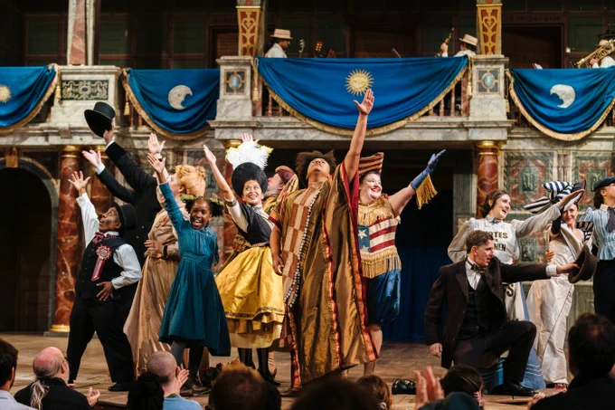 The Company of Princess Essex (2024). 

A vibrant performance at the Globe Theatre with actors in colourful period costumes, enthusiastically posing on stage in front of an audience. 