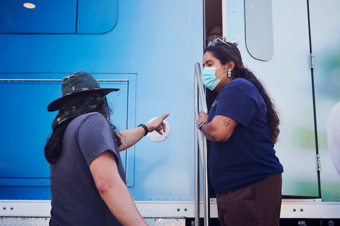 Two RFU members standing outside of the Care Coach. One of them is standing by the door, which is opened slightly, and the other is standing away and pointing to it.