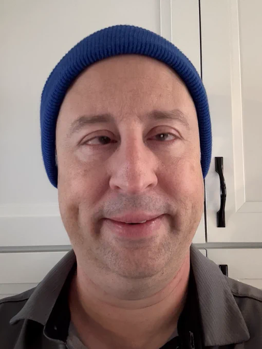 Level Access Chief Accessibility Officer Jon Avila smiles, wearing a navy blue beanie against a neutral background of white cabinetry. 