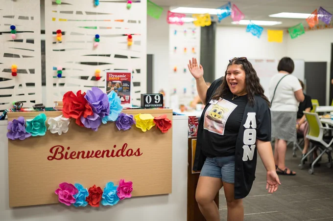 A Chico State student poses for a photo by the front desk of El Centro Resource Center. A sign on the front desk reads "Bienvenidos, " meaning welcome in Spanish.