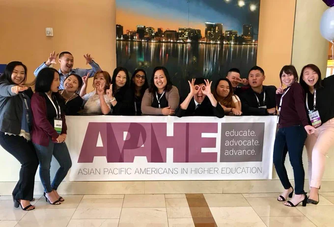 A group of students pose for a photo with a large banner that reads "Asian Americans in Higher Education".