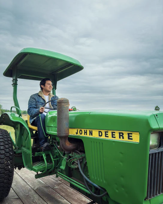 Joe Steven wearing a denim fleece jacket in an open field while riding a John Deere tractor.