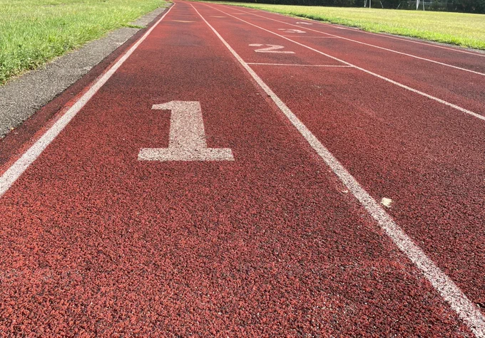 A run track with four lanes. The first one is in focus, the tarmac is red and the lines between the lanes are white, with big white numbers on each track. Photo by Aleksandar Pavlovic on Unsplasch
      