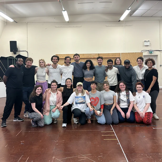 The company of A Midsummer Night's Dream in the rehearsal room standing and sitting in a big group