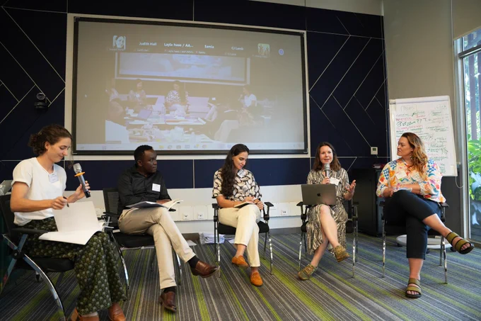 Panel discussion with five people listening to one person speak into a microphone.