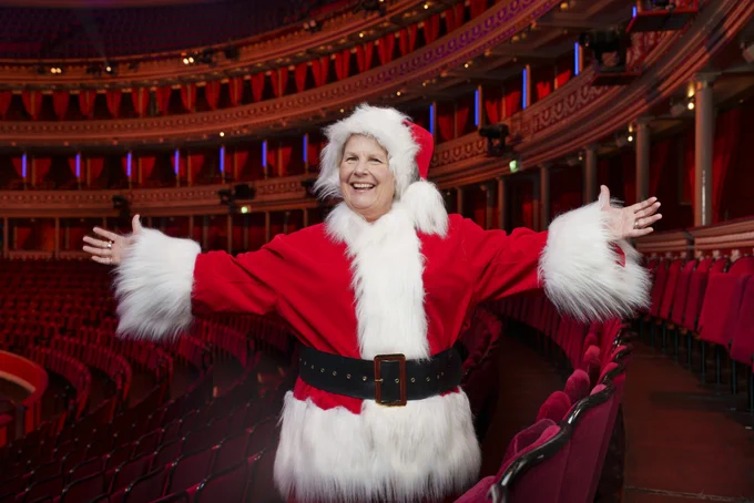Sandi Toksvig dressed in a Santa Claus costume standing with arms outstretched, smiling in the Royal Albert Hall.