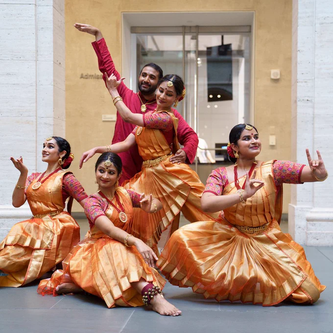 A group of bharata natyam dancers wearing red and gold clothing