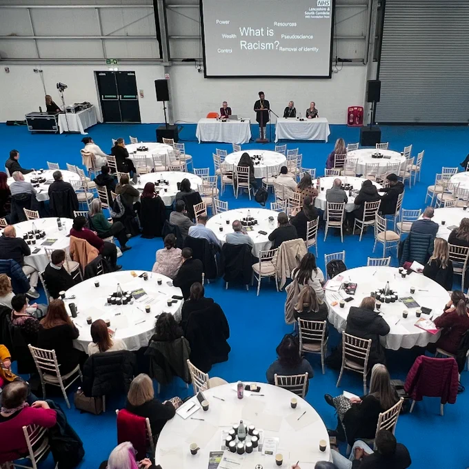 birds eye view of colleagues sat at tables looking at screen at the inclusion and belonging conference