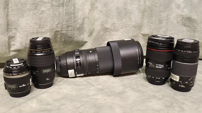 Five DSLR camera lenses are arranged in front of a gray backdrop.