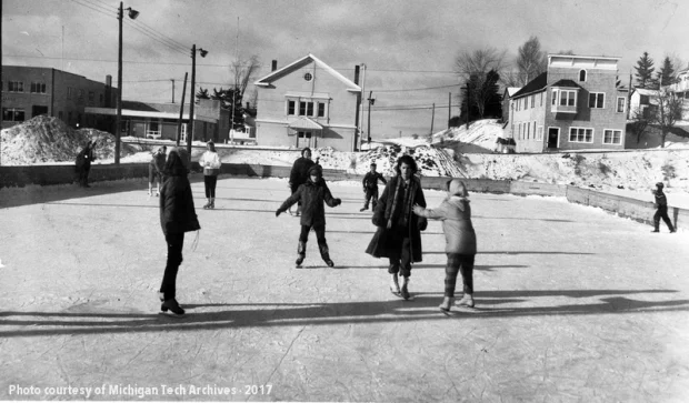 Group of people skating on a basic rink surrounded by various types of buildings